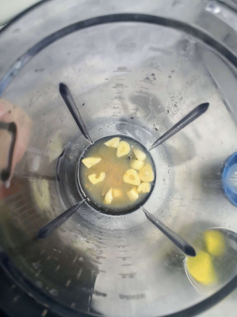 Aquafaba, garlic, lemon juice and salt in a clear blender looking down from above