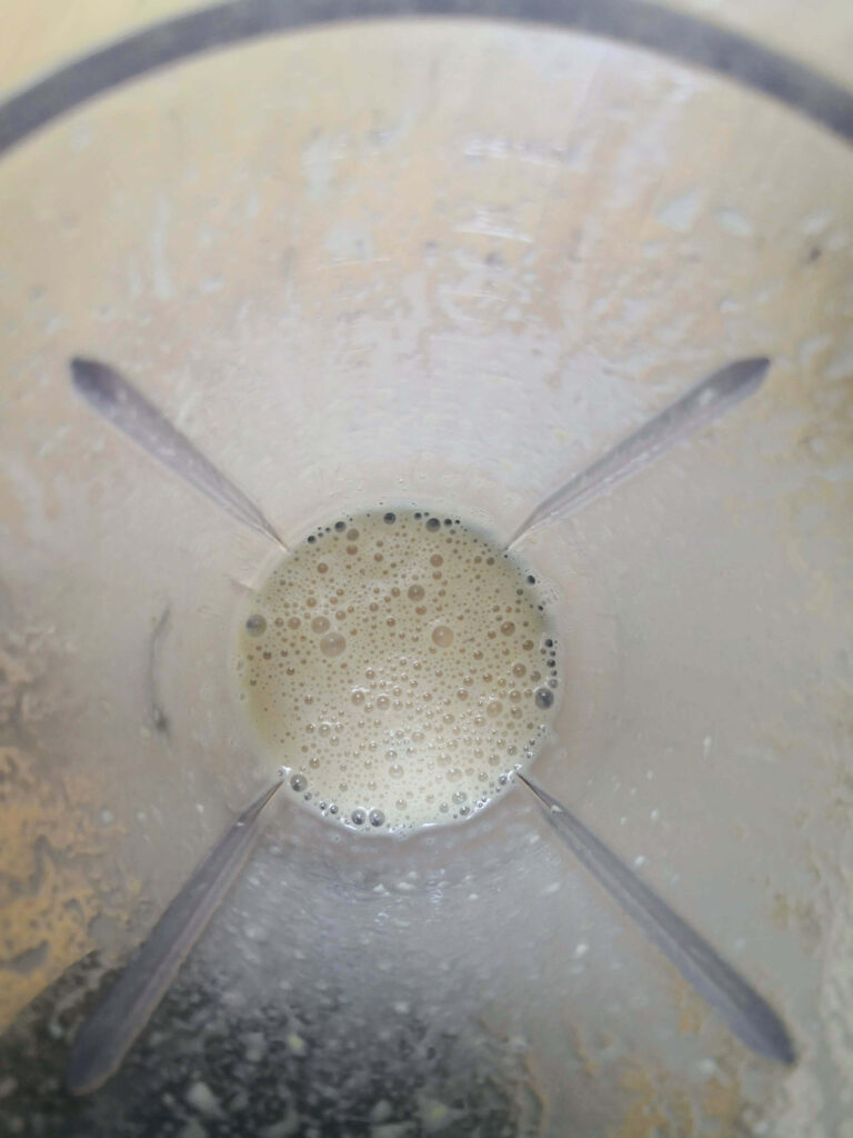 Frothy liquid aquafaba in clear sided blender looking down from above