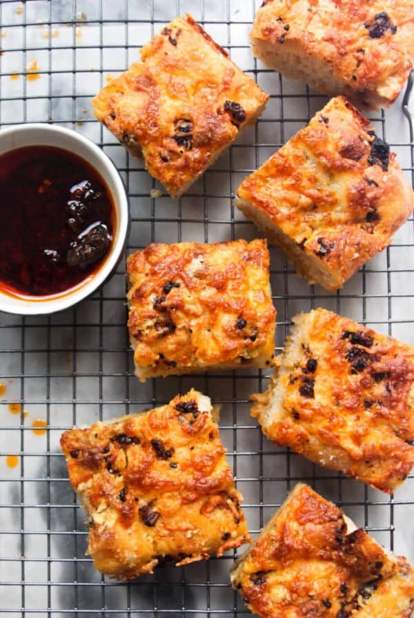 7 pieces of focaccia on a wire rack with a small bowl of chilli oil on the side.