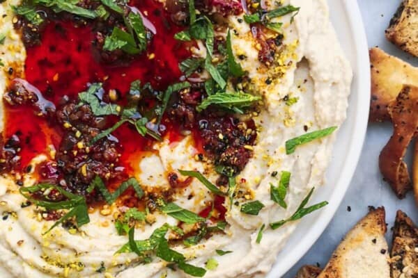 A small white plate of chilli oil topped super smooth hummus, with pita chips on the side.