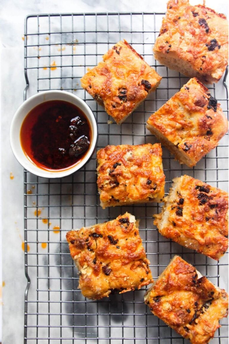 7 pieces of focaccia on a wire rack with a small bowl of chilli oil on the side.