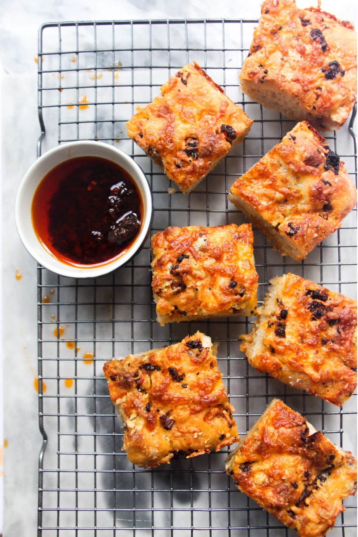 7 pieces of focaccia on a wire rack with a small bowl of chilli oil on the side.