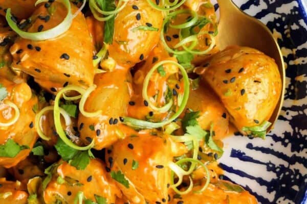 Orange gochujang potatoes in a white and blue bowl with small bowl of gochujang aioli on the side.