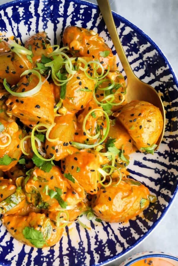 Orange gochujang potatoes in a white and blue bowl with small bowl of gochujang aioli on the side.