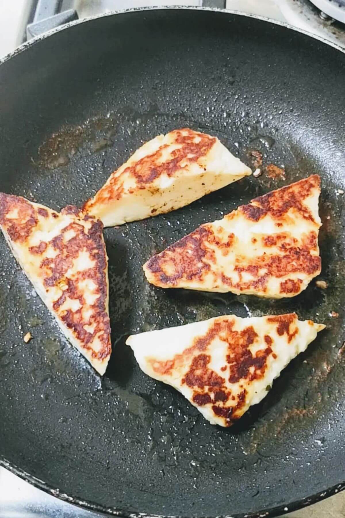 Four halloumi triangles frying in the pan