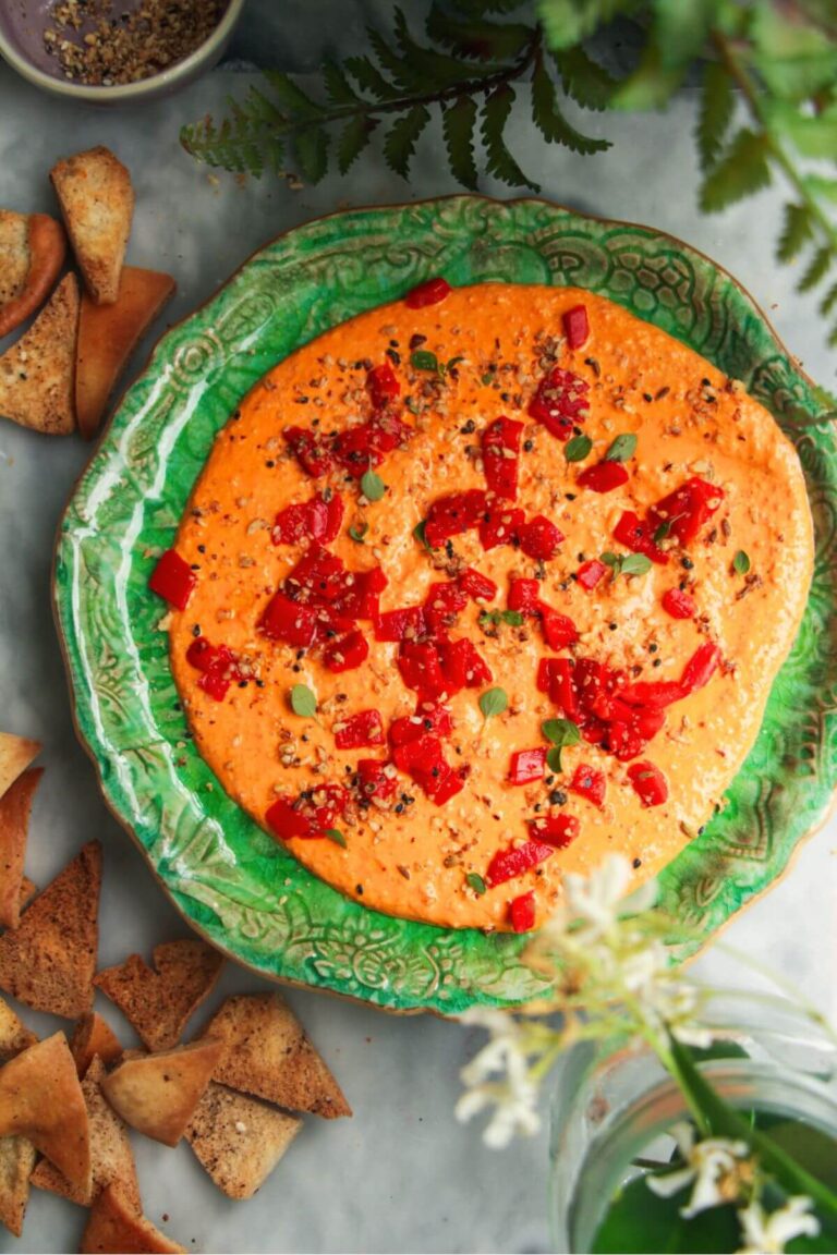 Red pepper feta dip on a small green plate with pita chips on the side.