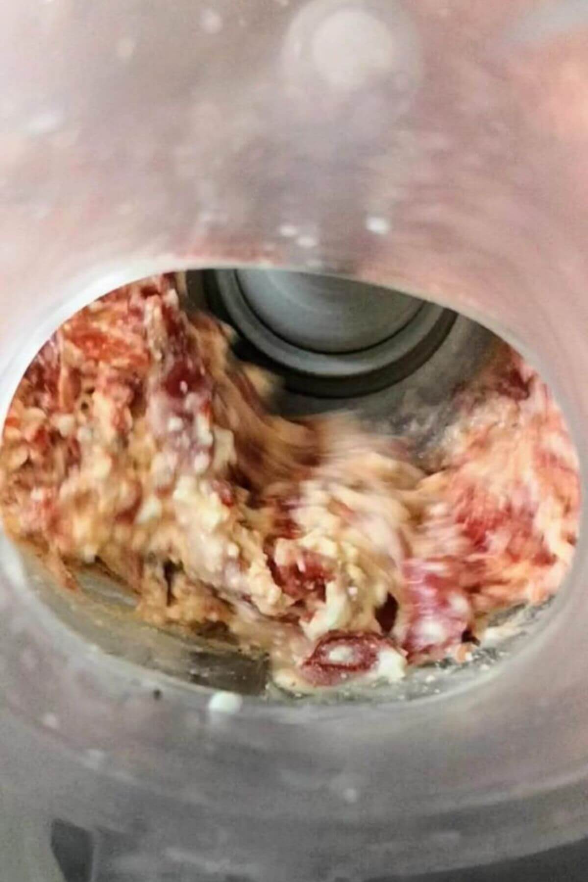 Blended up red pepper, feta, olive oil and lemon juice looking down into the bowl of a food processor from above