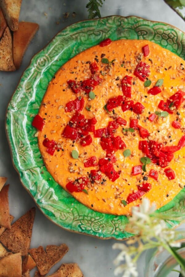 Red pepper feta dip on a small green plate with pita chips on the side.