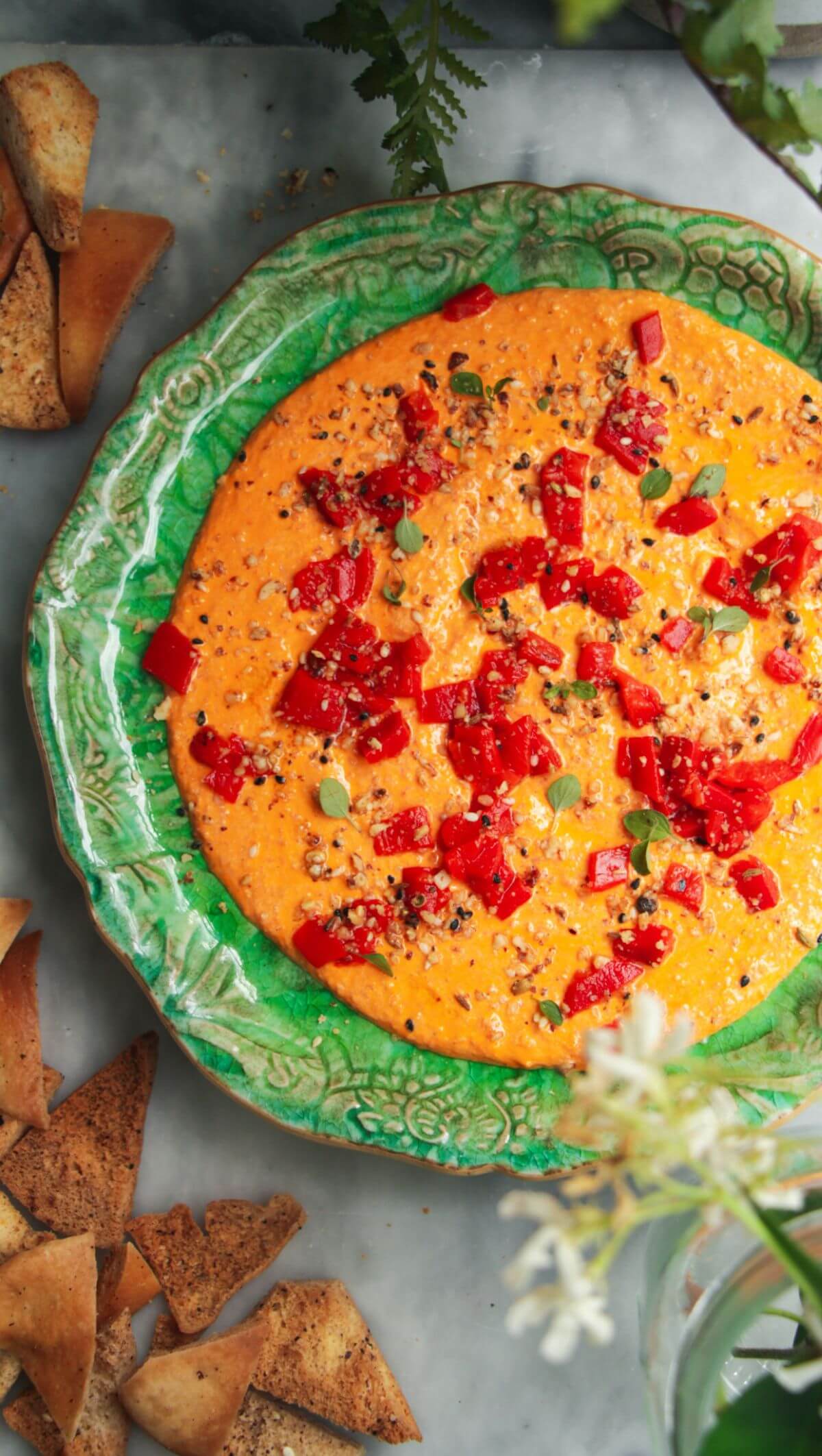 Red pepper feta dip on a small green plate with pita chips on the side.