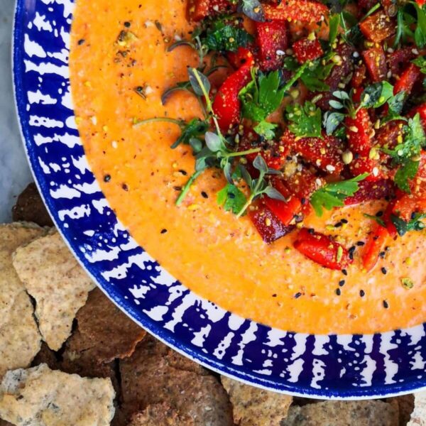 Red pepper and feta dip in a bowl with blue and white stripes, topped with red pepper, parsley and dukkah with crackers on the side
