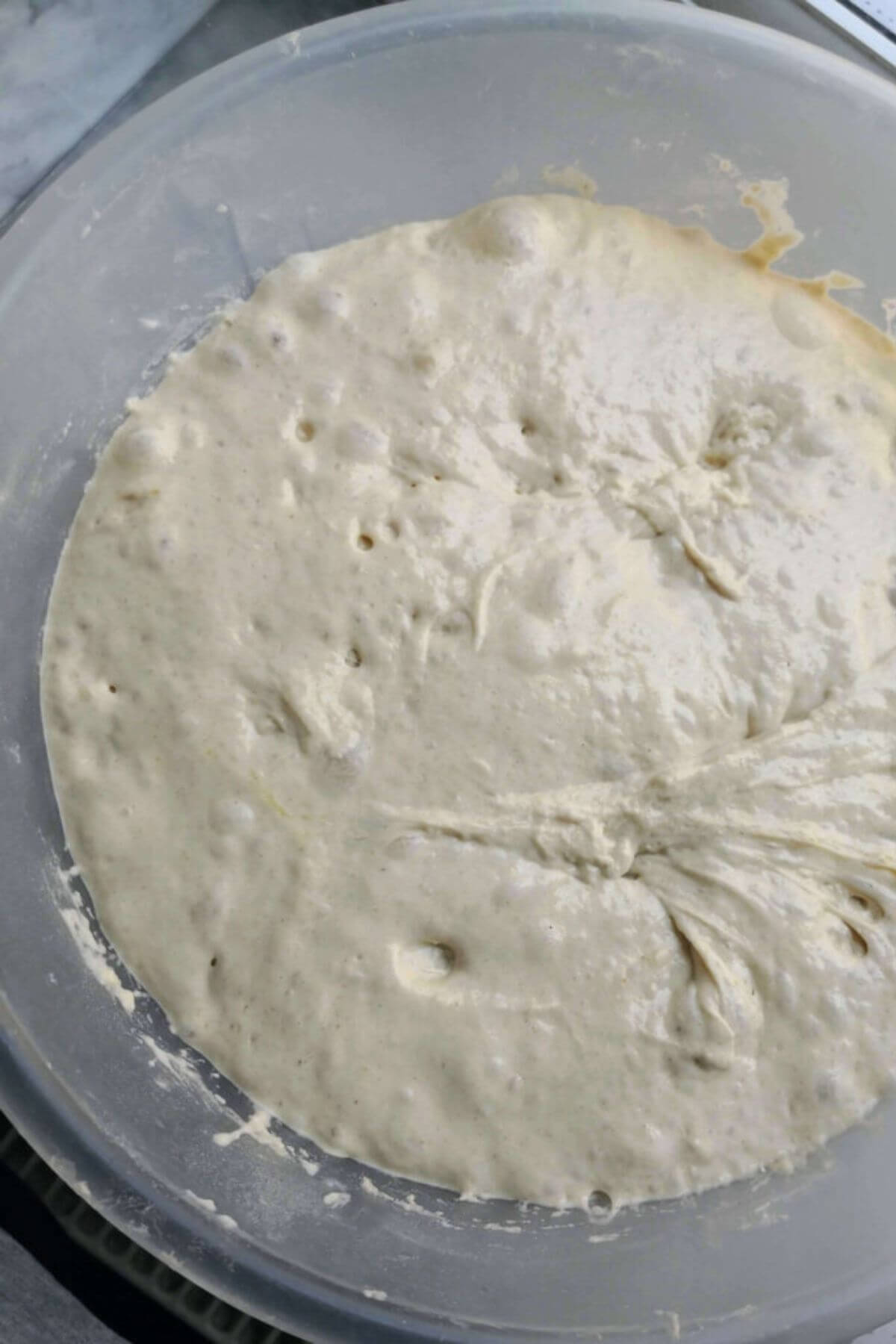 Focaccia dough after rising with lots of bubbles on top, in a large clear mixing bowl.