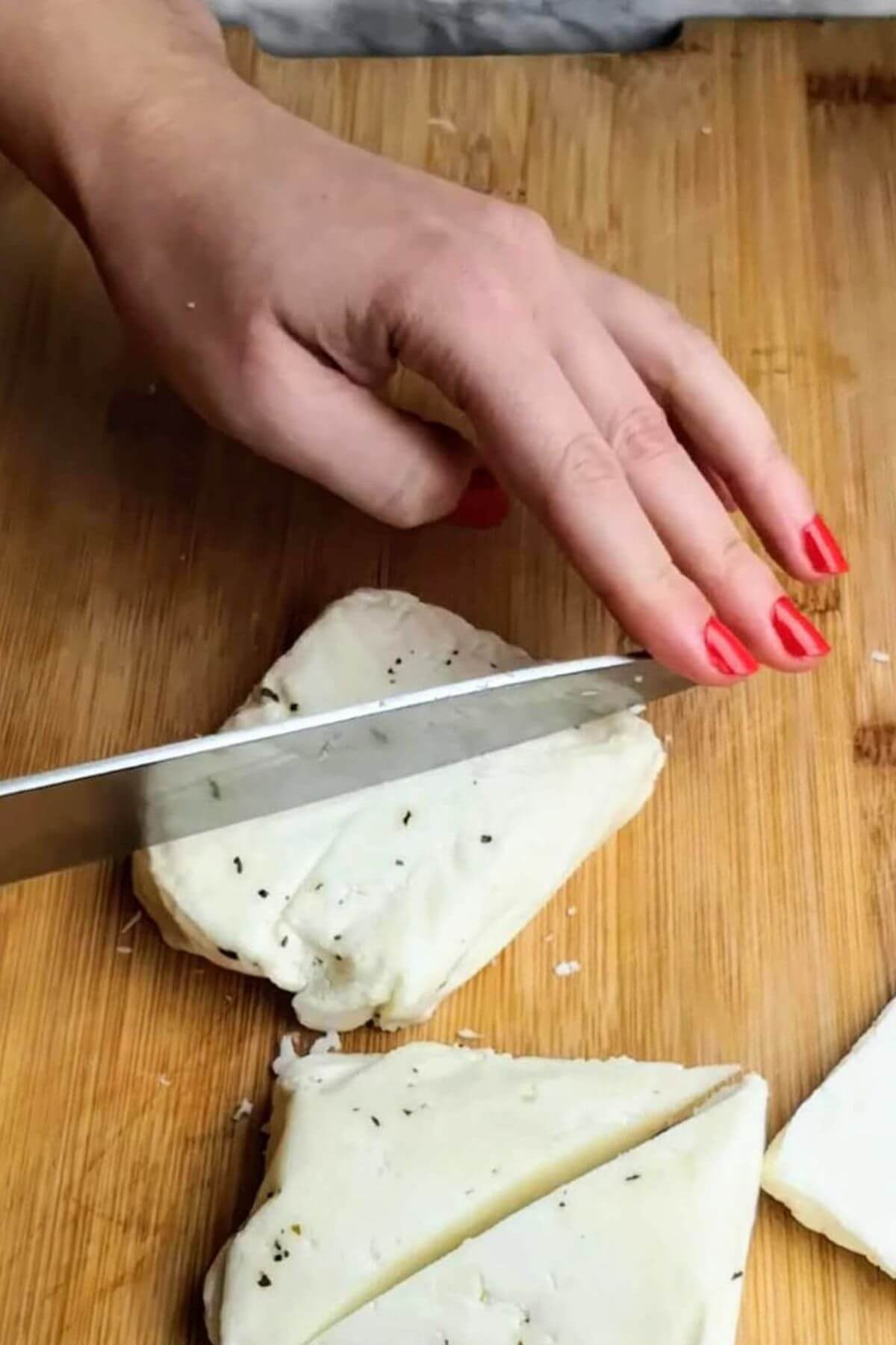Hand cutting large triangle of halloumi with a knife.