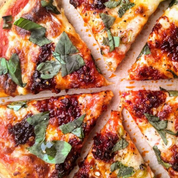 Nduja, spring onion and honey pizza sliced on a board.