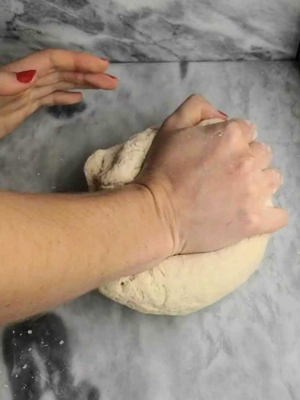 Different angle of a hand kneading the easy soft flatbread dough on a grey marble background.