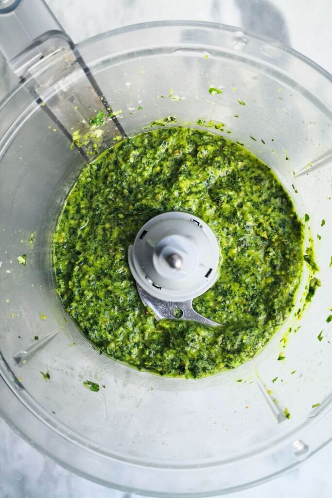 Blitzed basil pesto in the bowl of a food processor.