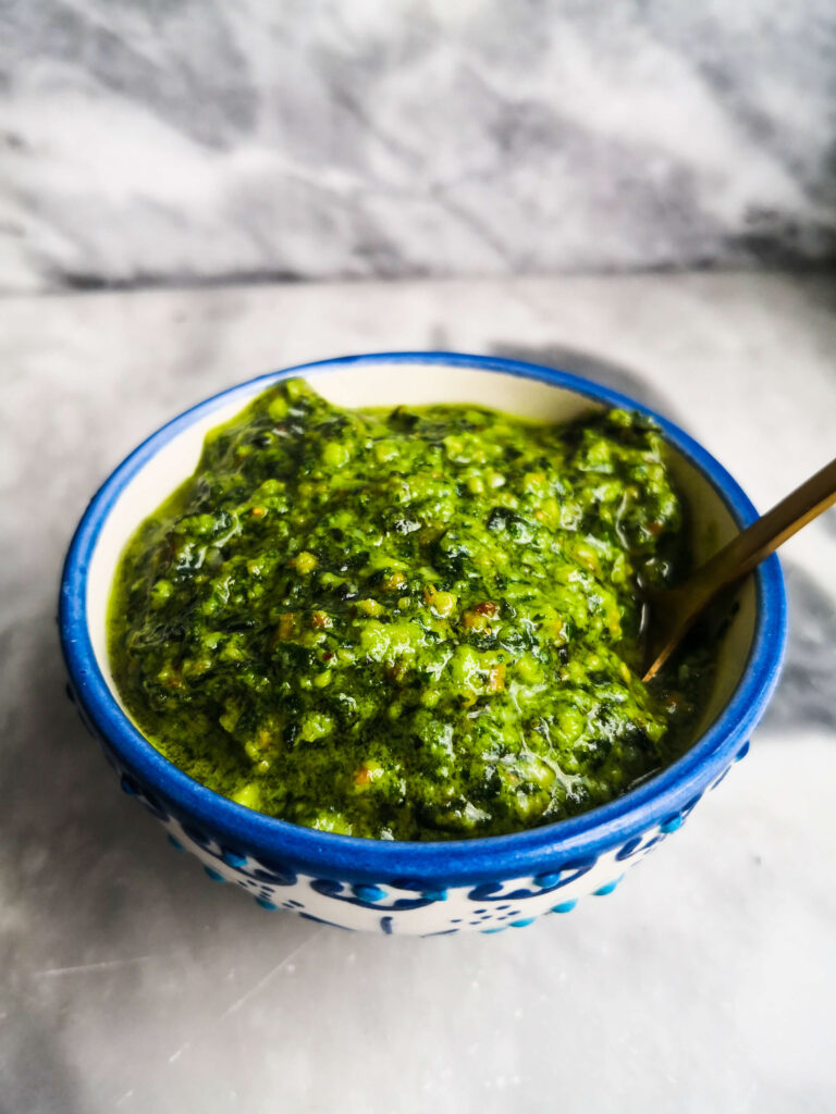 Homemade basil pesto in a small white and blue bowl on a grey marble background.