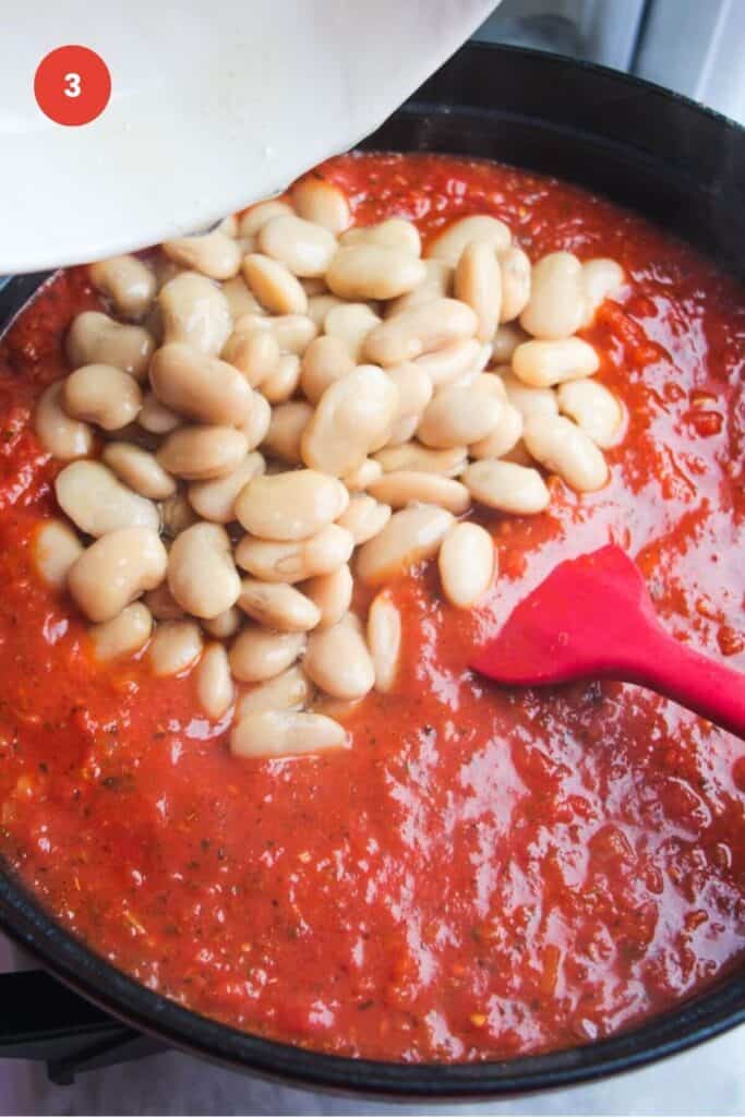 White beans added to tomato sauce in a large pan.