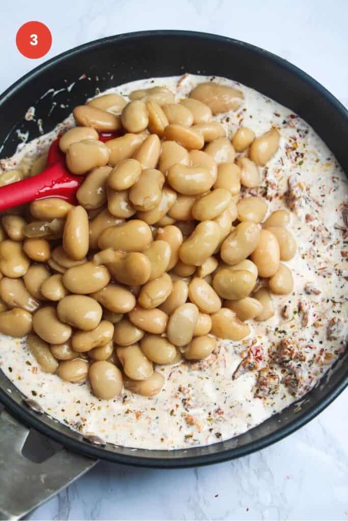 White beans added to creamy sauce in a skillet.
