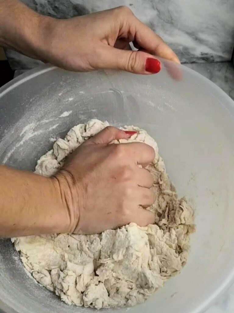 A hand pressing down on the easy soft flatbread dough in a large clear mixing bowl.