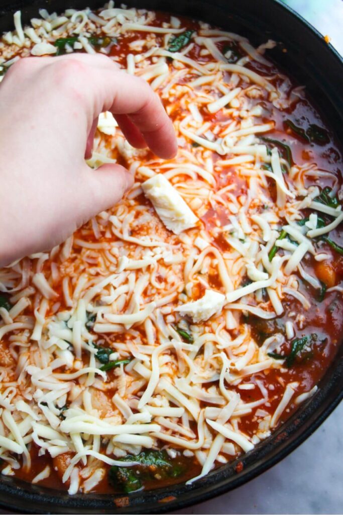 Adding cheese on top of white beans in a tomato sauce.
