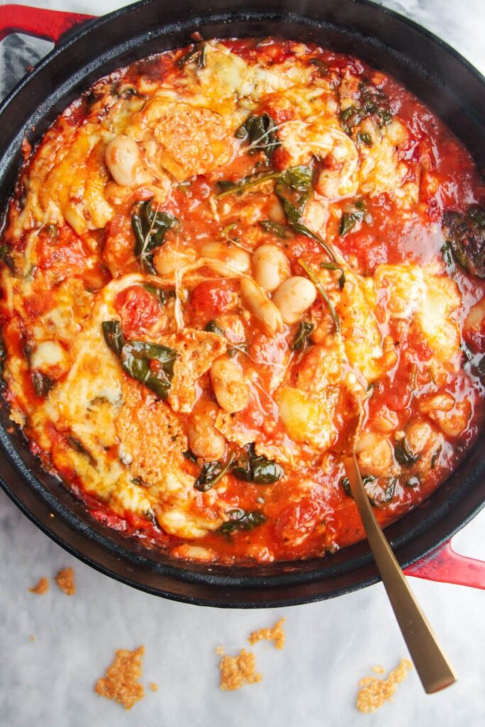 Cheesy white beans in tomato sauce in a large black pan on a grey marble background.