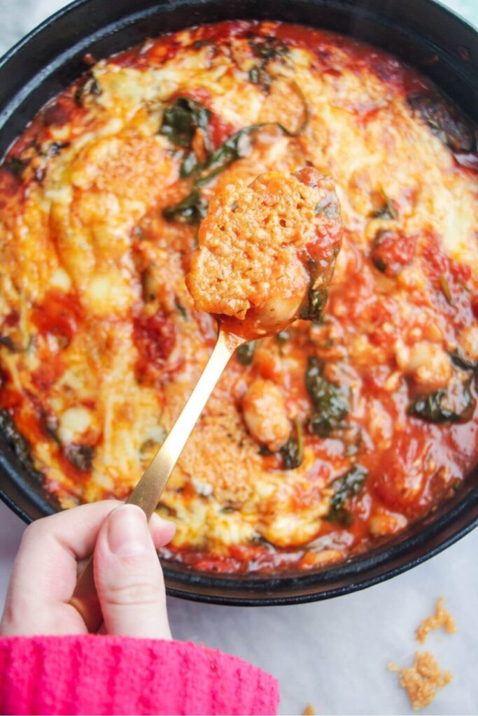 Hand holding up a spoon with cheesy tomatoey baeans on it.