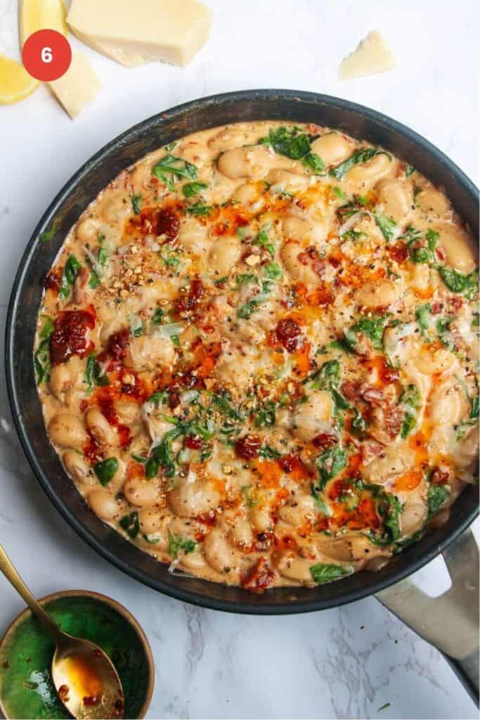 Chili oil and parmesan on top of creamy white beans in a skillet.