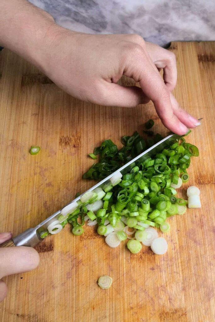 Chopping scallions on a large wooden board with a large knife.
