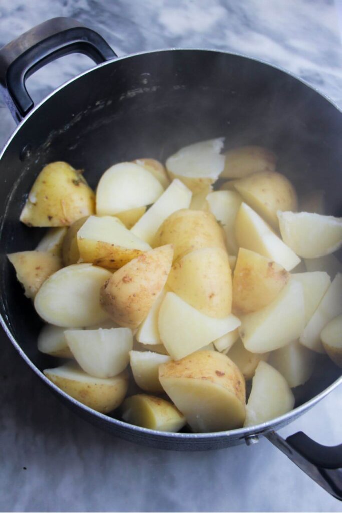 Par-boiled potatoes in a large black pot.