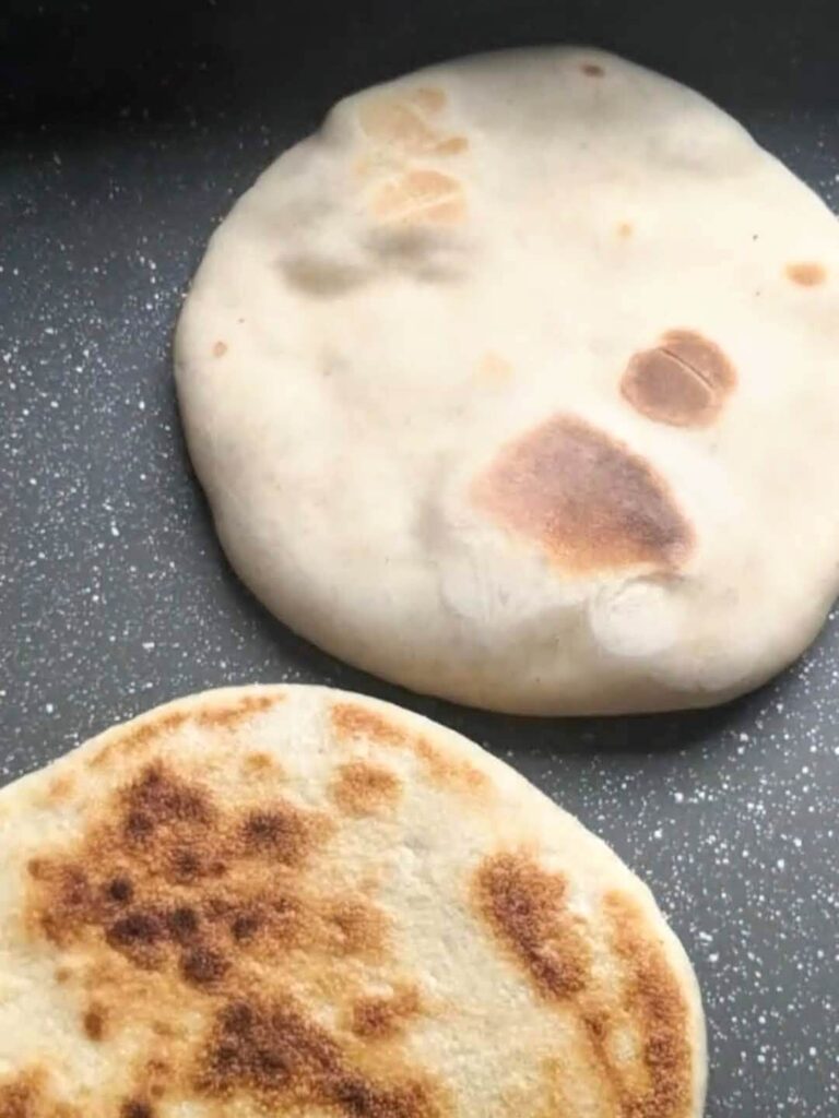 Two flatbreads in a pan with golden spots on either side.