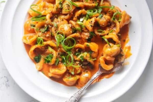 Creamy gochujang pasta topped with green coriander & spring onions on a white plate with a sliver spoon.