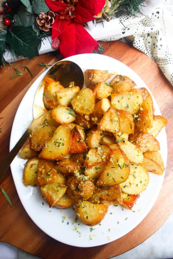 Crispy golden potatoes on a white oven plate with large gold spoon on a wooden background.