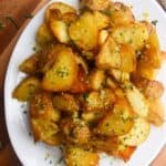 Crispy golden potatoes on a white oven plate with large gold spoon on a wooden background.