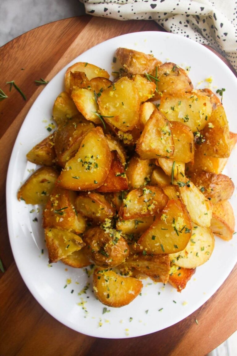 Crispy golden potatoes on a white oven plate with large gold spoon on a wooden background.
