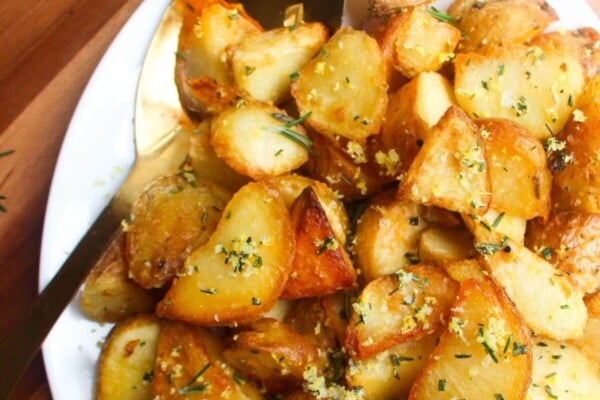 Crispy golden potatoes on a white oven plate with large gold spoon on a wooden background.