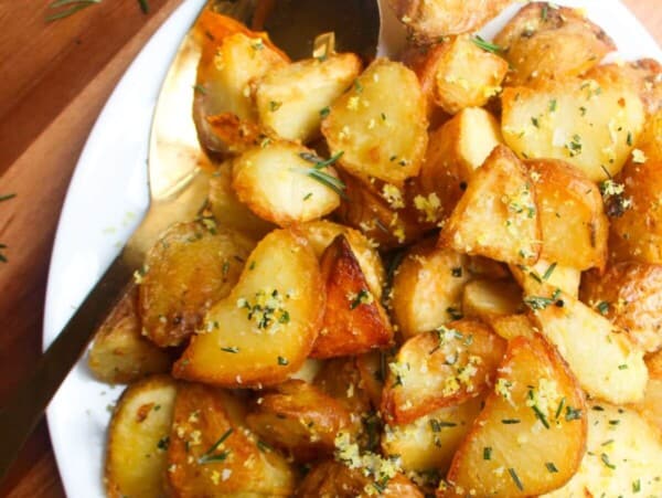 Crispy golden potatoes on a white oven plate with large gold spoon on a wooden background.