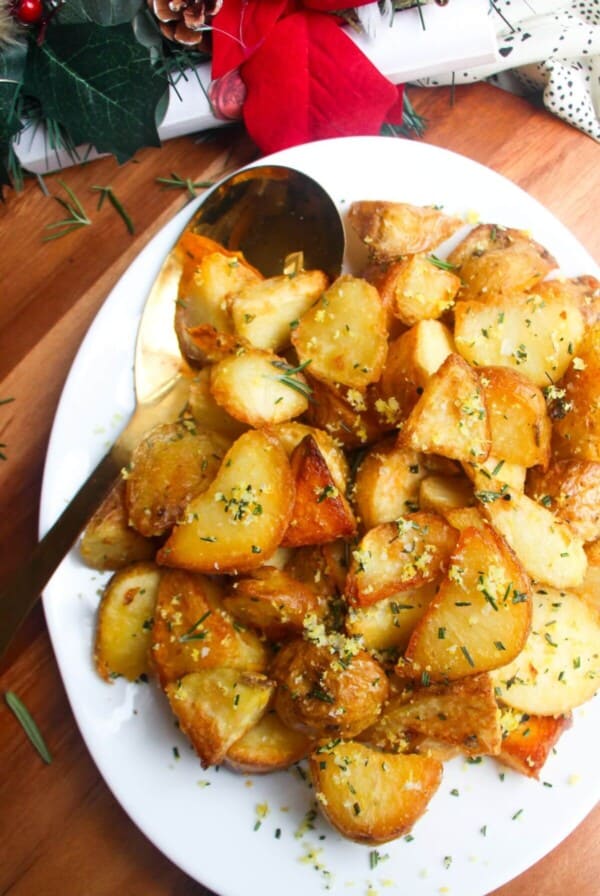 Crispy golden potatoes on a white oven plate with large gold spoon on a wooden background.