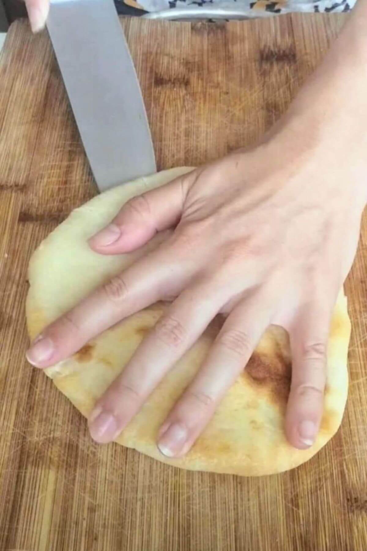 Cutting a pita bread in half on a wooden board.