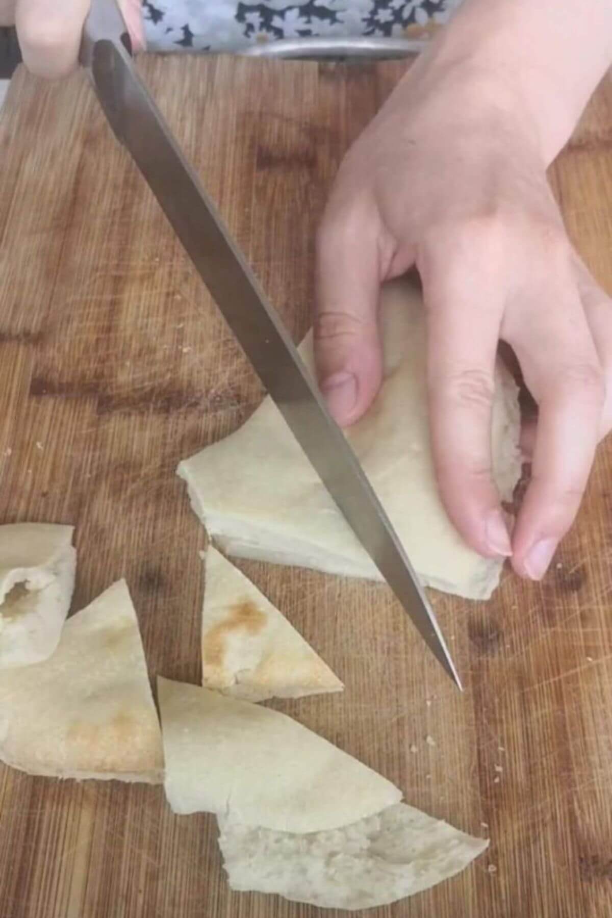 Hand holding knife and cutting pita bread into triangles.