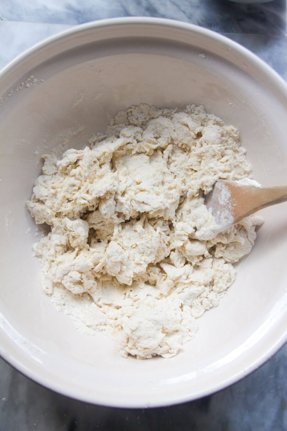 Rough, shaggy dough after being mixed with a large wooden spoon in a large ceramic bowl.
