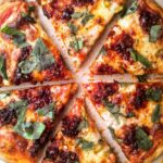 Easy homemade pizza cut into slices, topped with 'nduja, basil, spring onion and mozzarella.