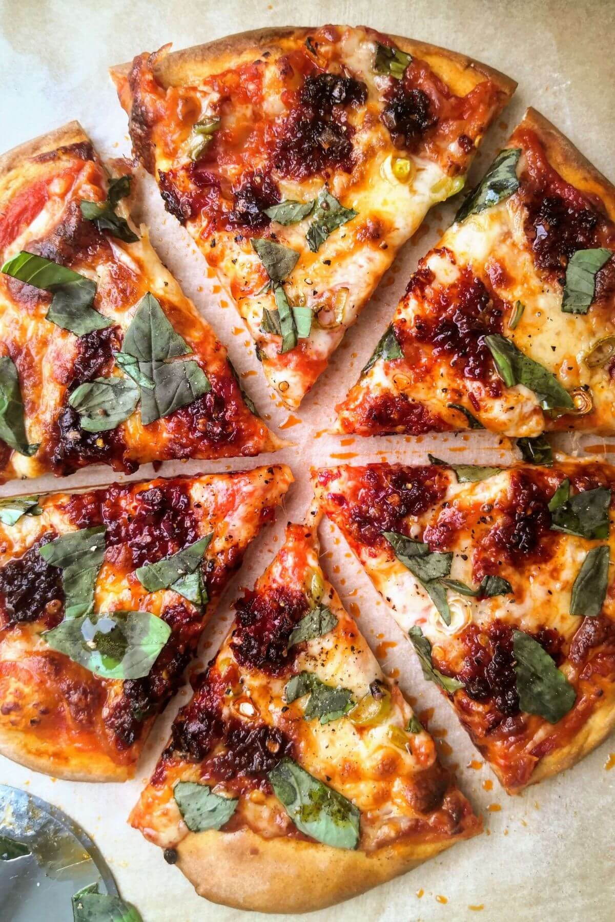 Easy homemade pizza cut into slices, topped with 'nduja, basil, spring onion and mozzarella.