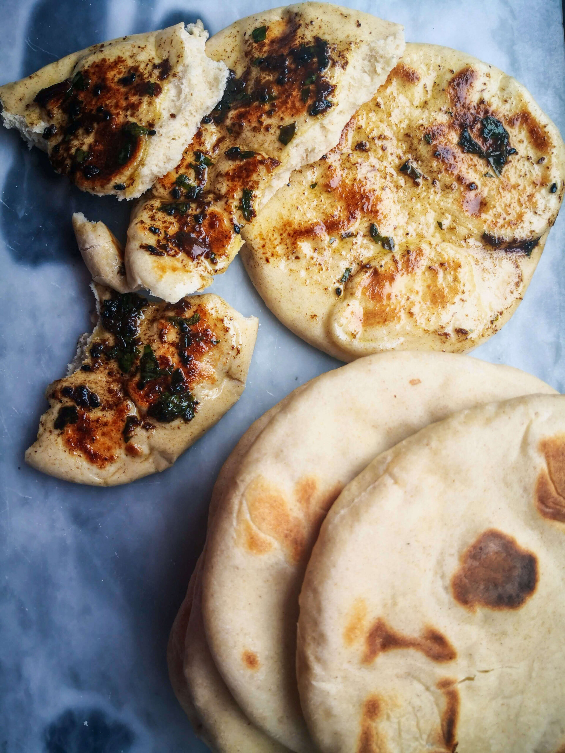 A pile of easy soft flatbreads with garlic butter on a grey marble background.