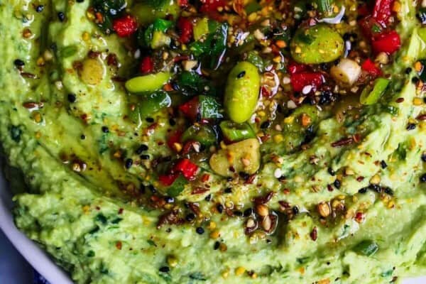 Edamame hummus with avocado on a small white plate, with pita chips on the side.