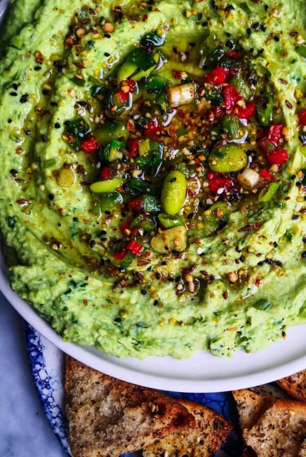 Edamame hummus with avocado on a small white plate, with pita chips on the side.