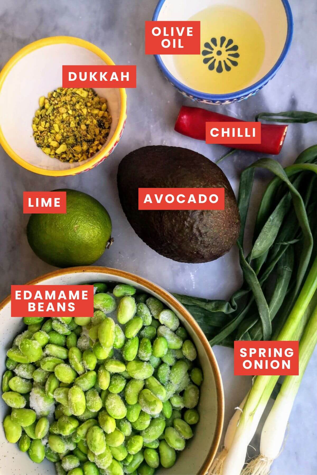 Ingredients for edamame hummus with avocado on a grey marble board.