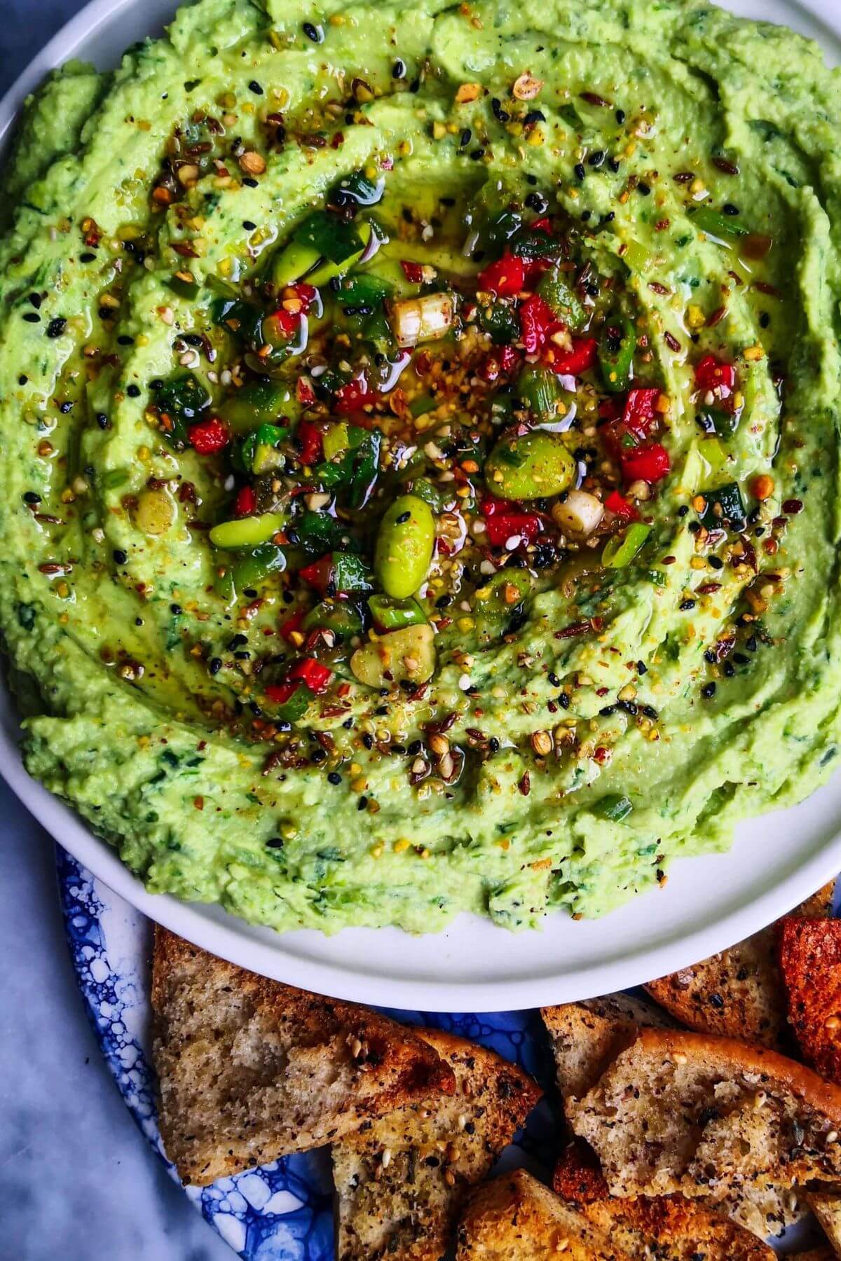 Edamame hummus with avocado on a small white plate, with pita chips on the side.