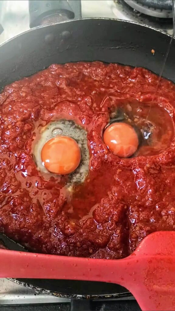 Two eggs sitting in holes in the shakshuka sauce in a small black pan.