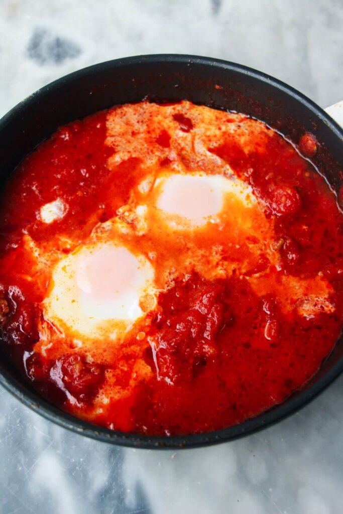 Cooked eggs in tomato sauce in a small black pan.