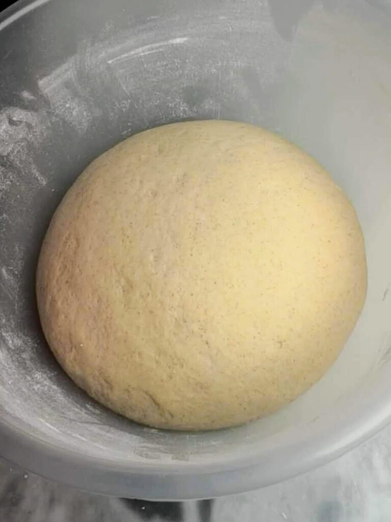 Easy soft flatbread dough puffy after rising in a large clear mixing bowl.